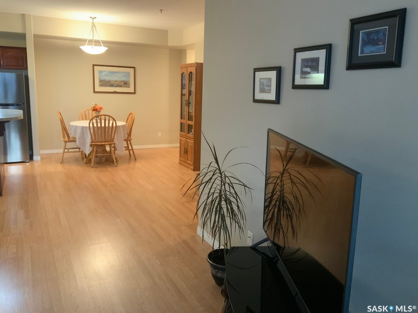 Light wood-finish flooring throughout, stainless steel refrigerator, recessed lighting, and a pendant light fixture