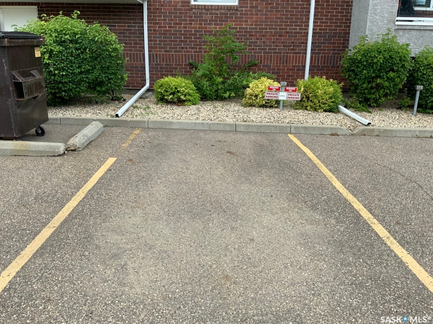 Paved parking area with painted lines, concrete curb, and a landscaped bed featuring shrubs and gravel
