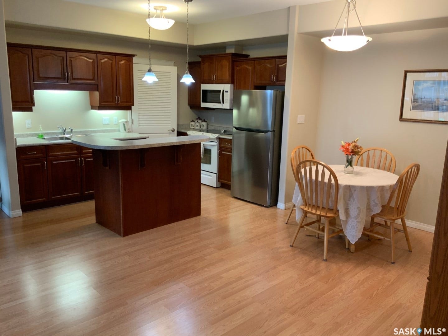Kitchen featuring wood-finish flooring, dark wood cabinetry, a breakfast bar, and stainless steel refrigerator