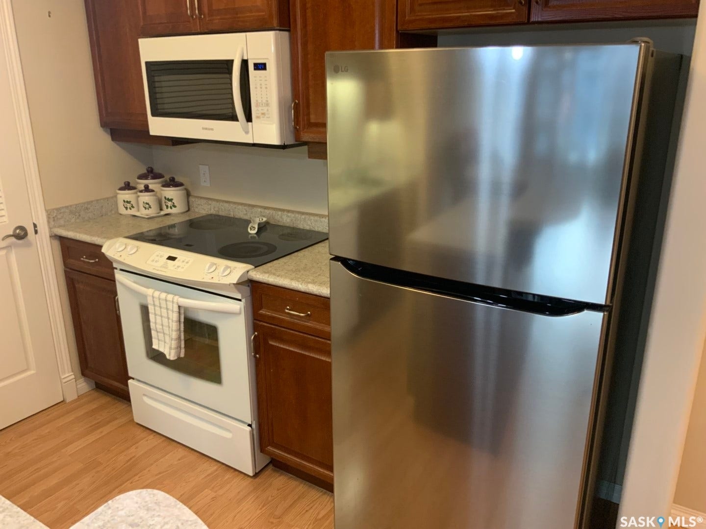 Stainless steel refrigerator, built-in microwave, dark wood-finish cabinetry, white range, and light-toned countertops