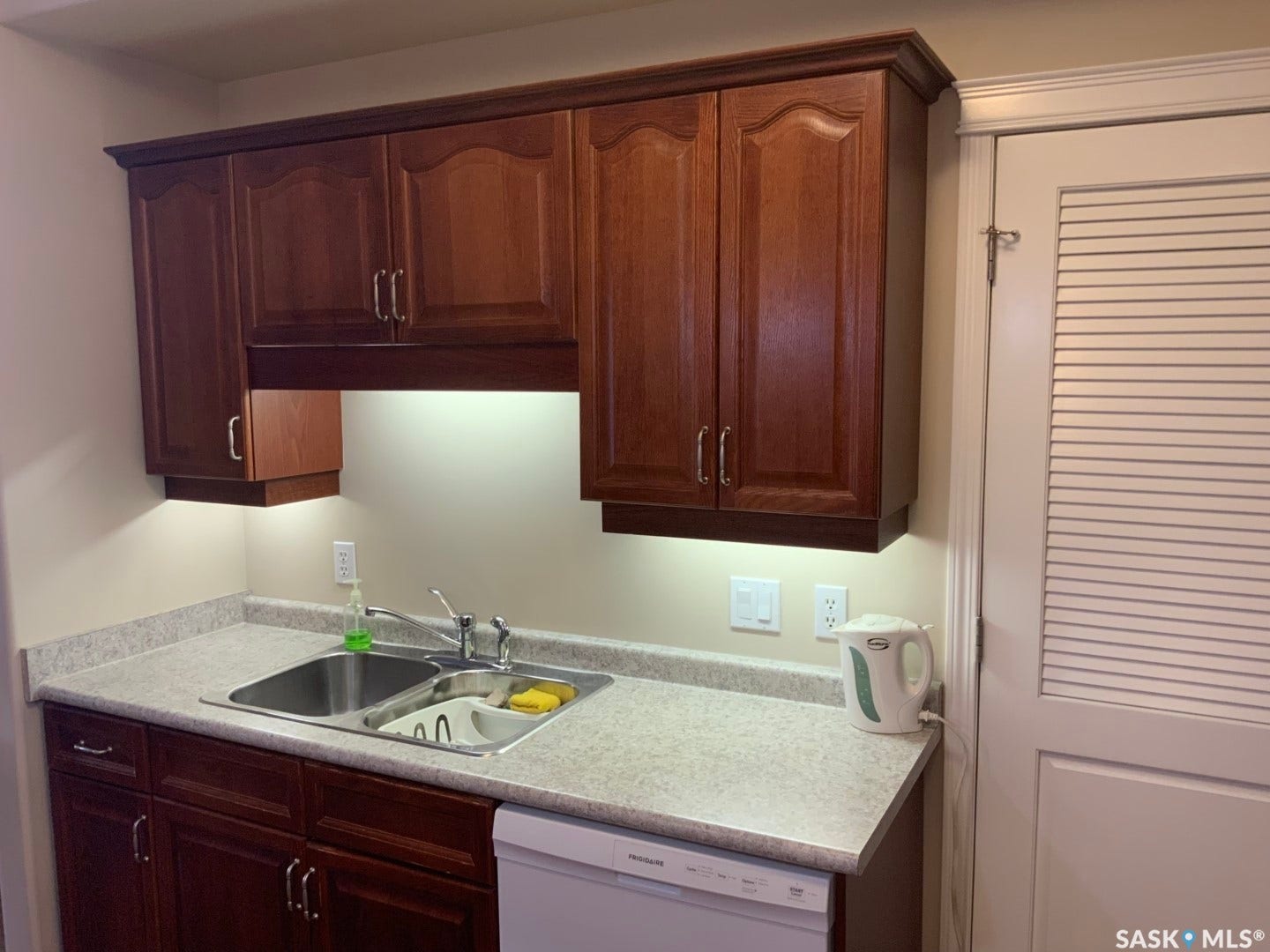 Wood-finish cabinetry with crown molding, double basin stainless steel sink, laminate countertops, and under-cabinet lighting