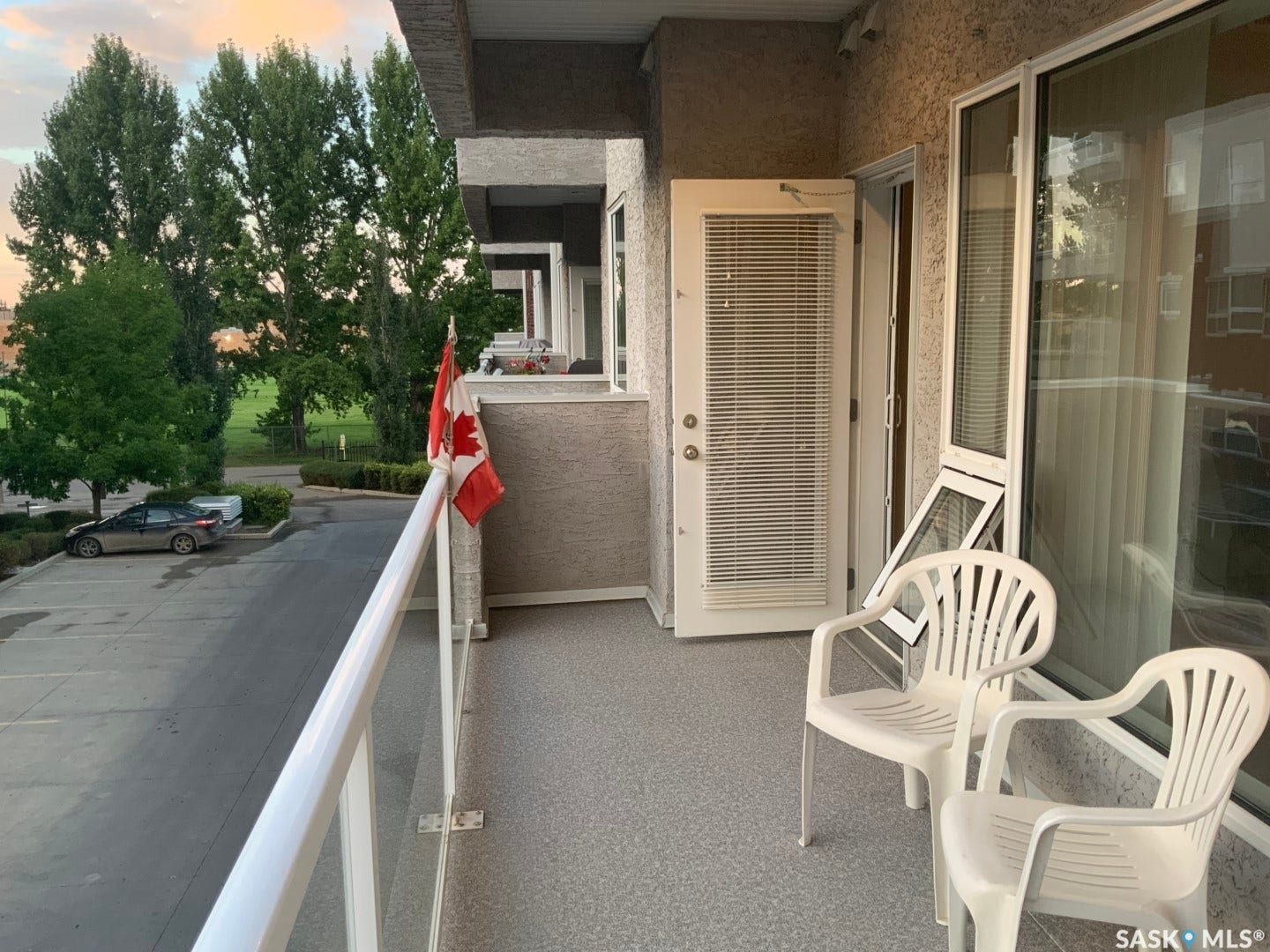 Balcony with textured flooring, glass panel railing, exterior door with integrated blinds, and adjacent large window