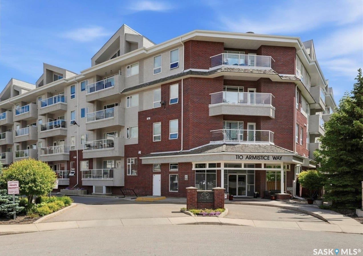 Multi-story building featuring brick and stucco exterior, multiple private balconies with glass railings, an inviting main entrance with a covered awning, and an established landscaped entrance