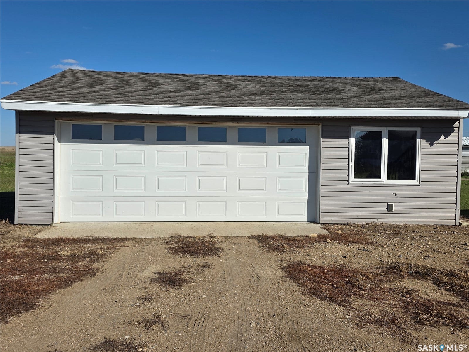 Gray horizontal siding with a white garage door featuring upper window panels, and a shingled roof