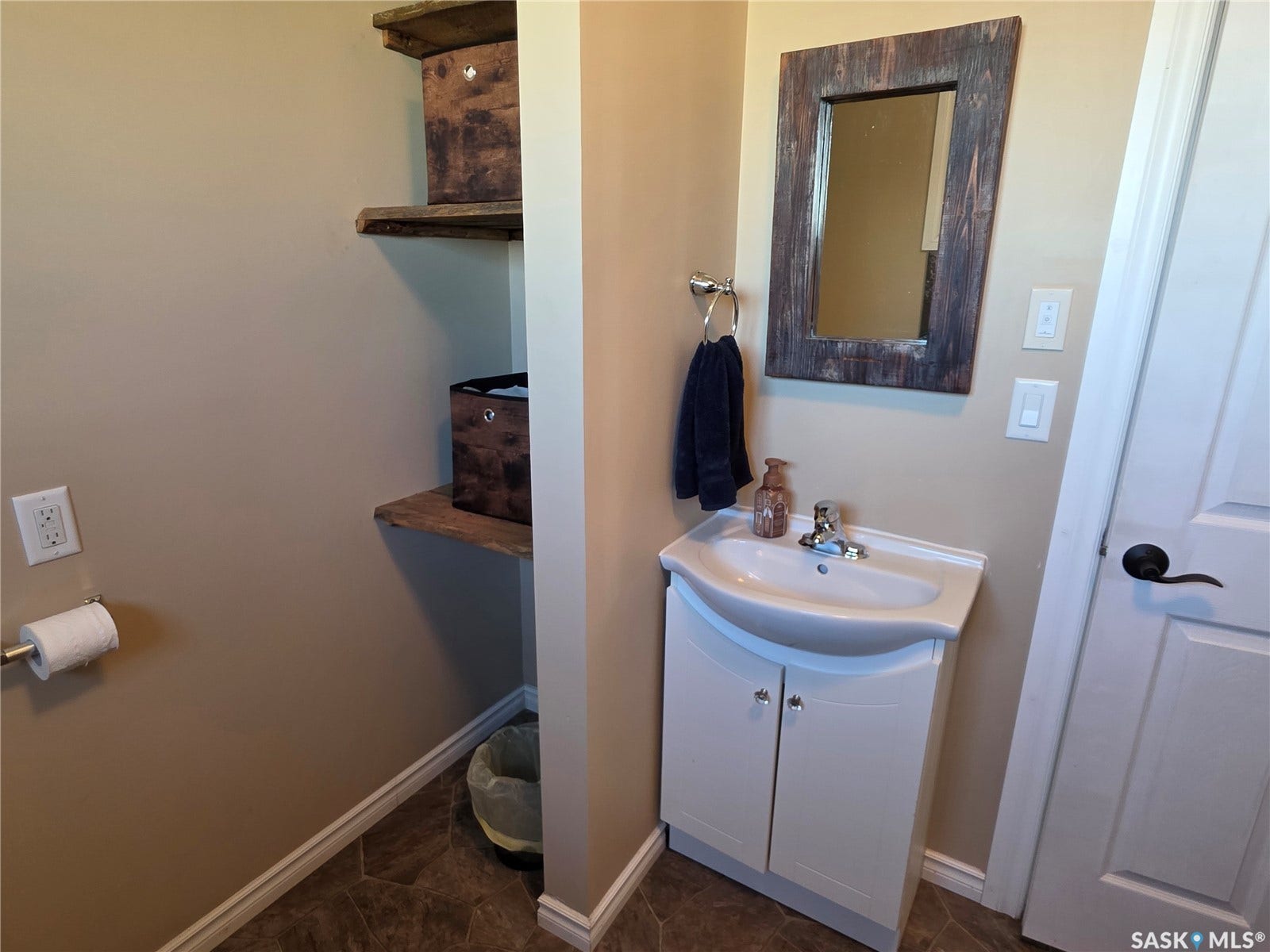 Wall-mounted shelving with wood-finish planks, white vanity with integrated sink, and a decorative framed mirror