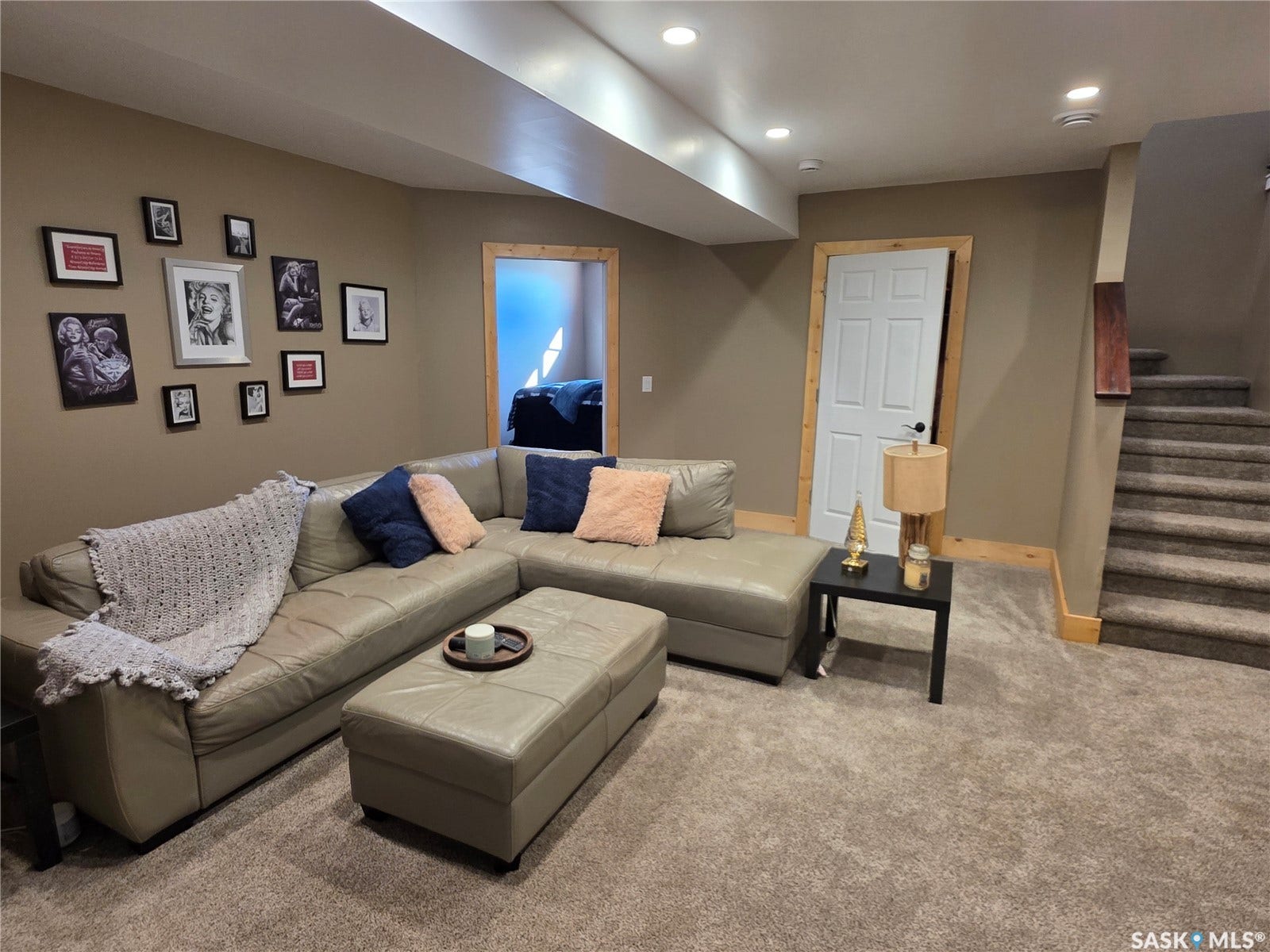 Recessed lighting illuminates the space, featuring a neutral color palette, wood-trimmed door, and a carpeted staircase with wood railing