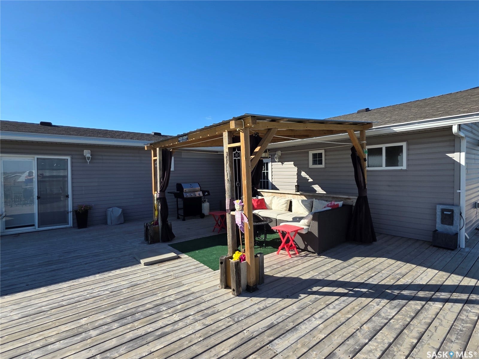 Expansive wood-finish deck with a built-in pergola, gray horizontal siding, and multiple windows