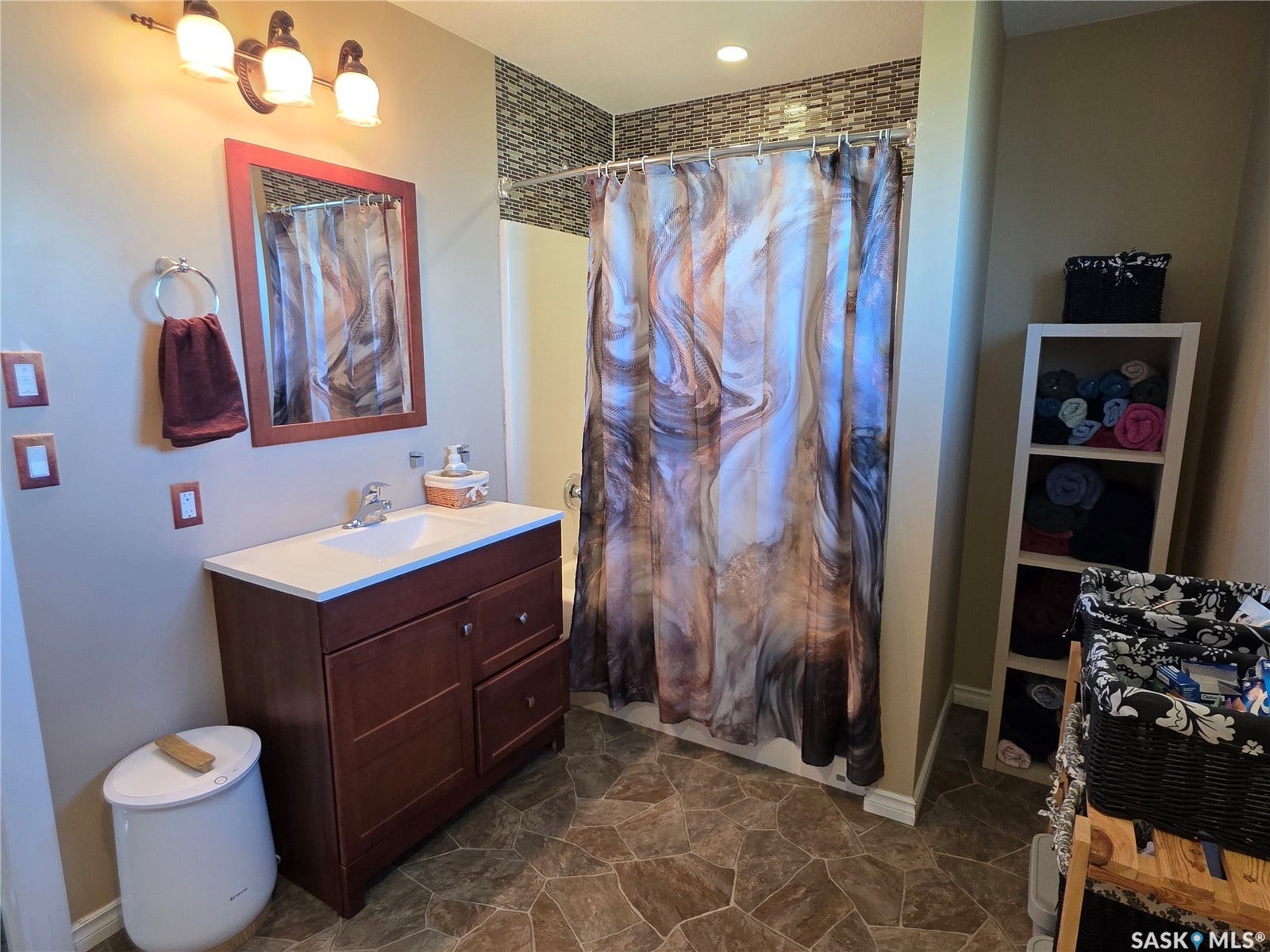 Vanity with a white countertop and integrated sink, framed mirror, wall-mounted light fixture, shower surround, and lino flooring