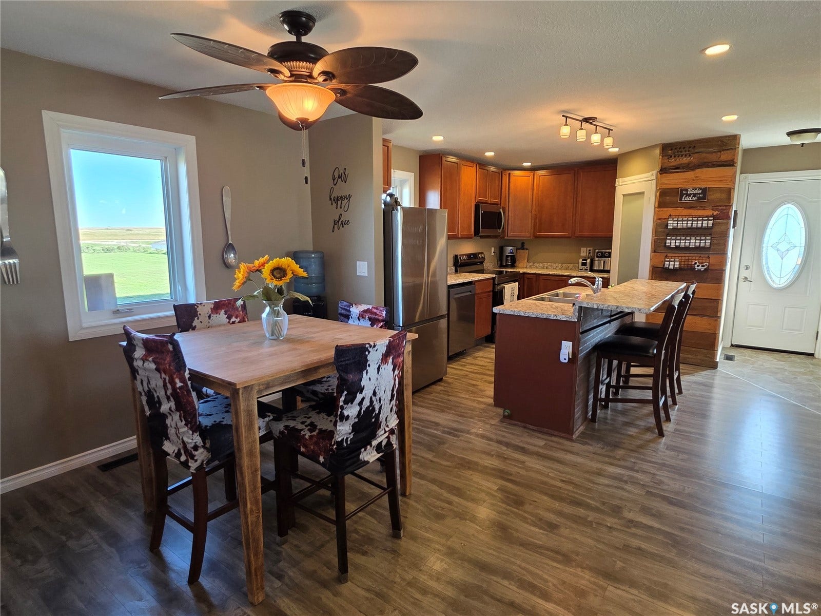 Open-concept kitchen with laminate flooring, stainless steel appliances, and a central island featuring a sink and seating