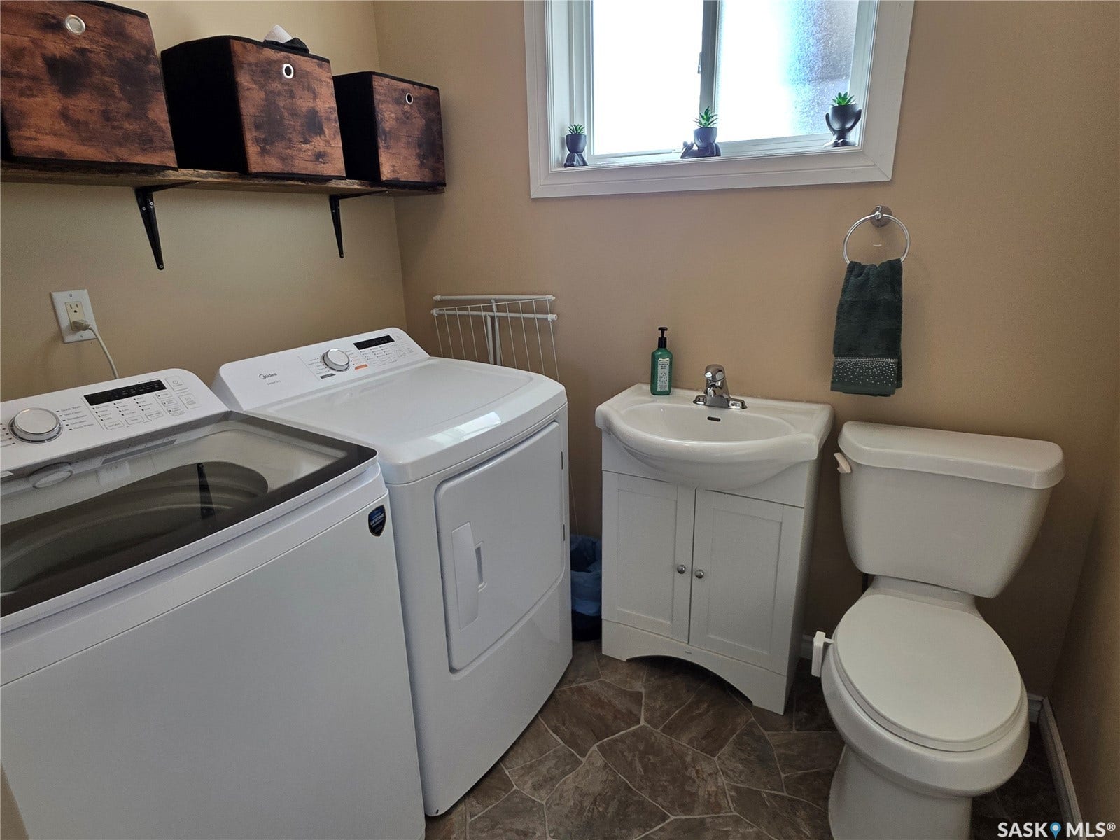Laundry space with a white top-load washer and dryer, adjacent to a white vanity with an integrated sink and a toilet