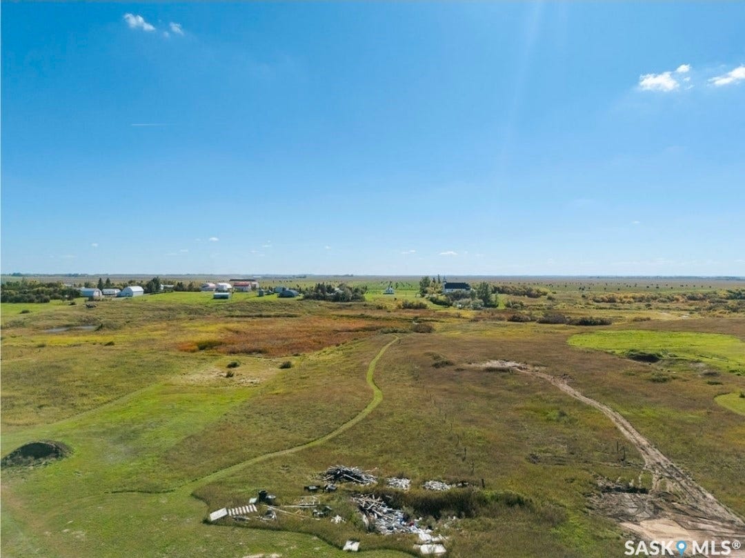 Expansive rural landscape featuring a mix of green and brown foliage with distant structures and clear sky