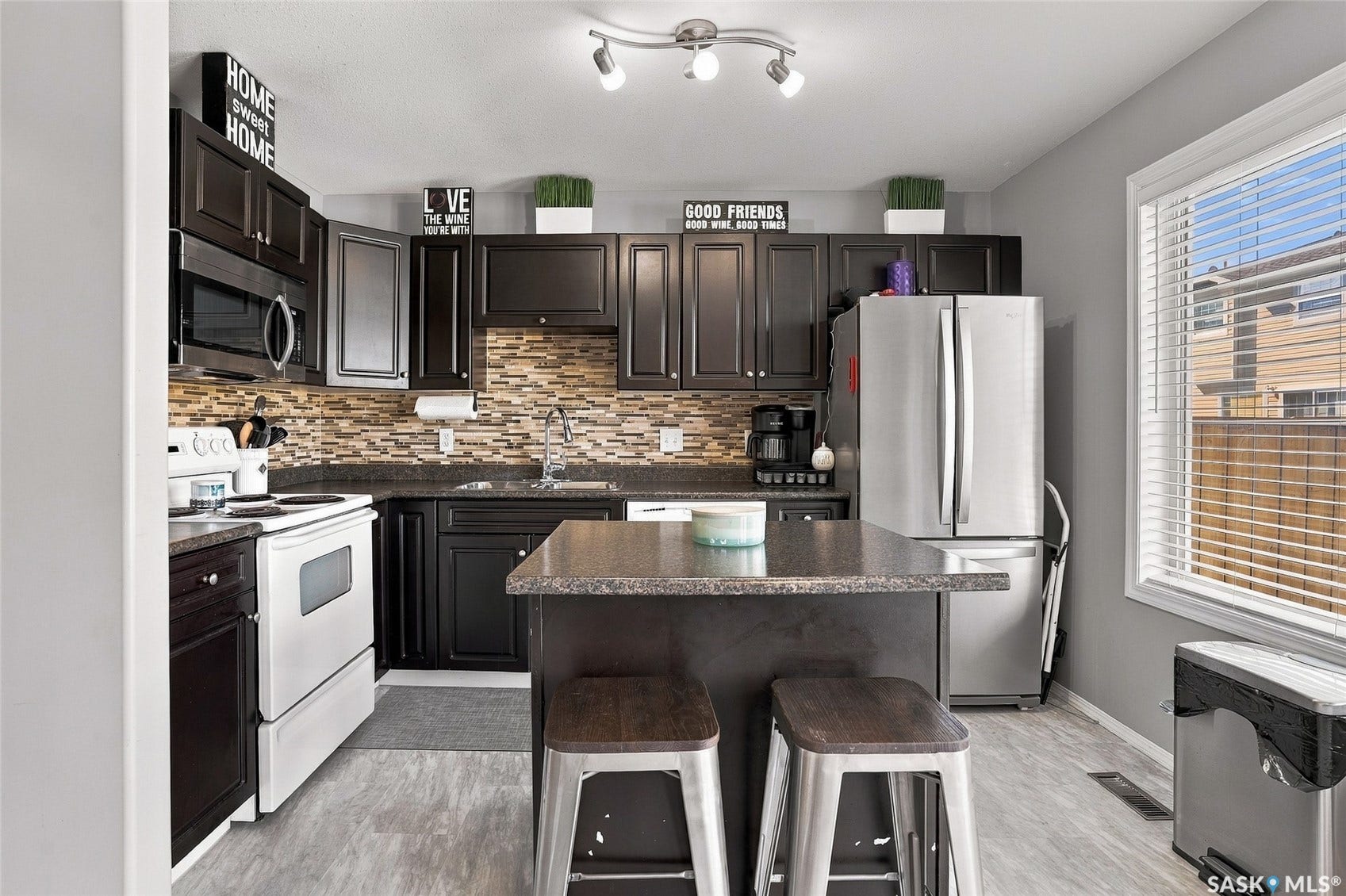Kitchen featuring dark wood-finish cabinetry, stainless steel appliances, a tile backsplash, light wood-finish flooring, and a center island with seating