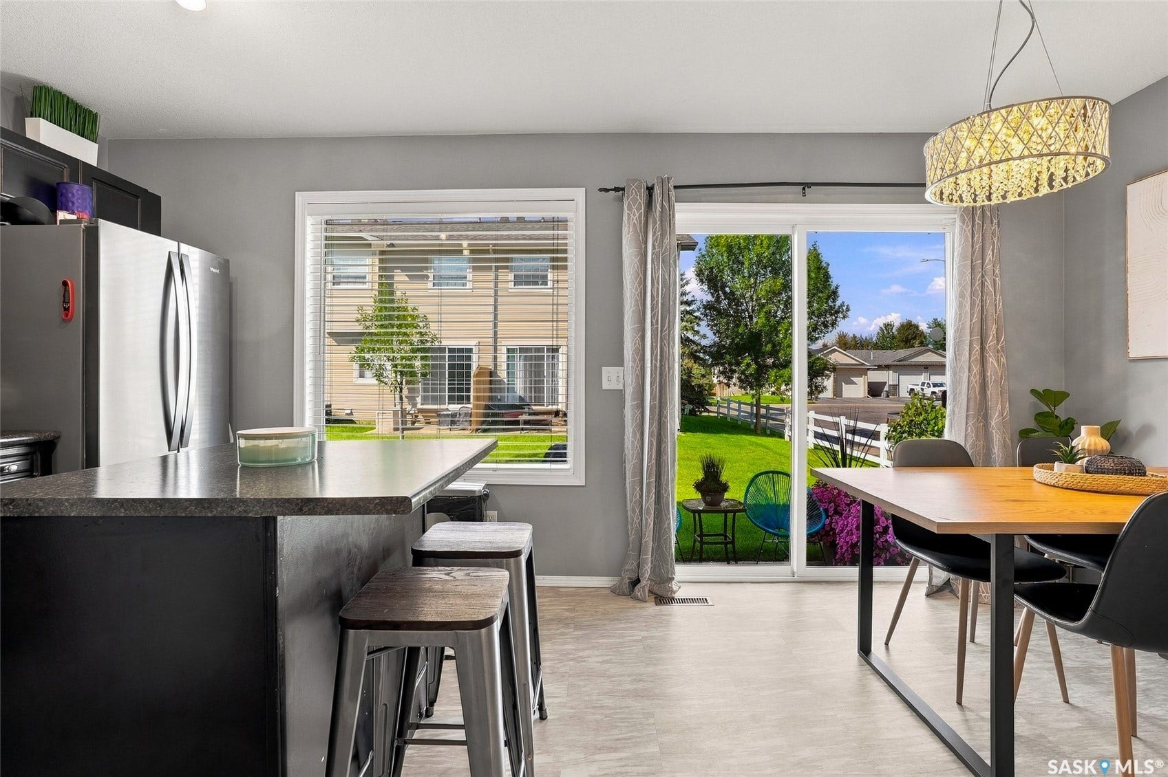 Kitchen island with seating, stainless steel refrigerator, contemporary dining chandelier, sliding glass door, and a backyard with a manicured lawn