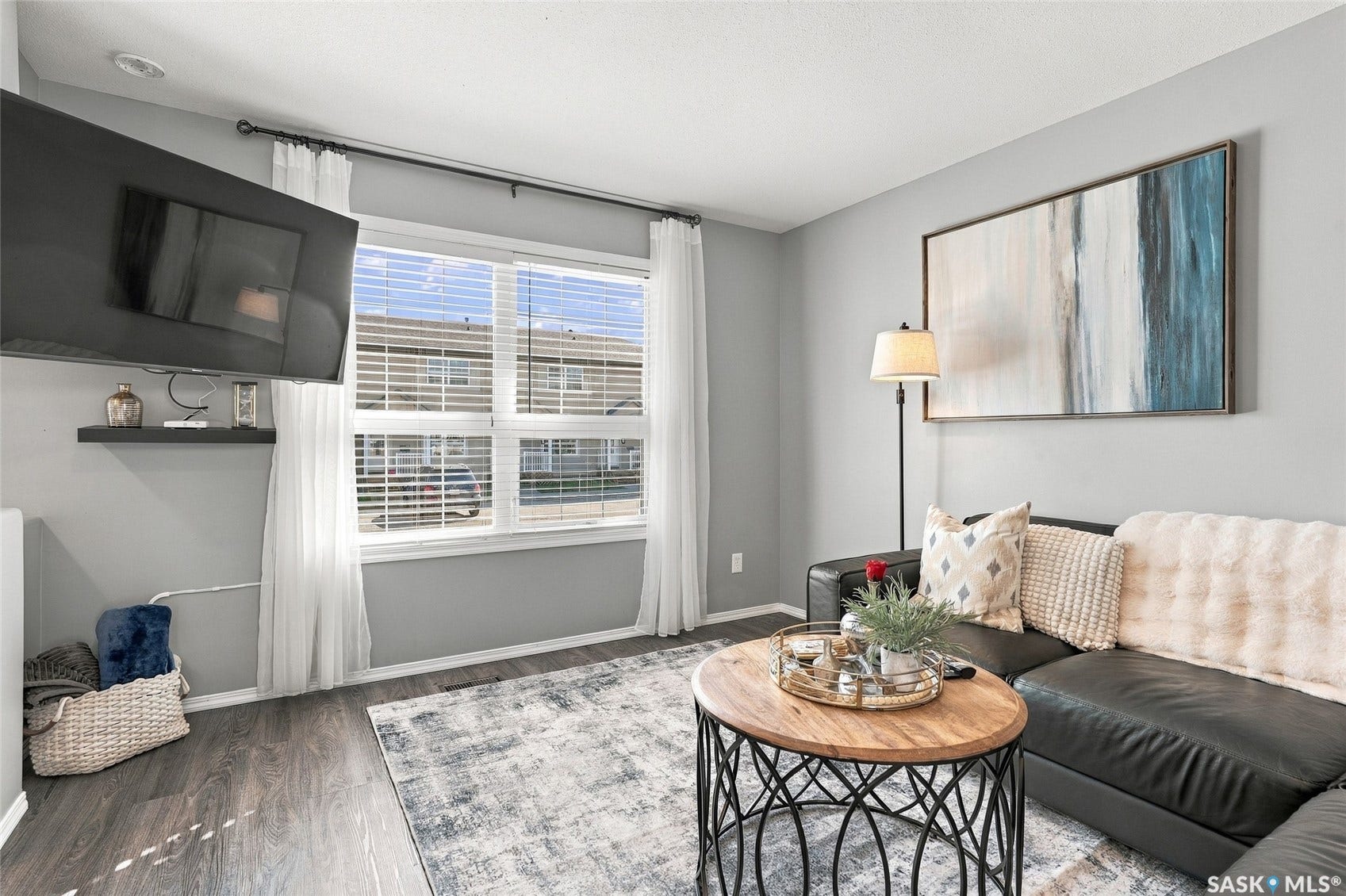 Hardwood-style flooring, large window with blinds, wall-mounted television, and neutral wall tones