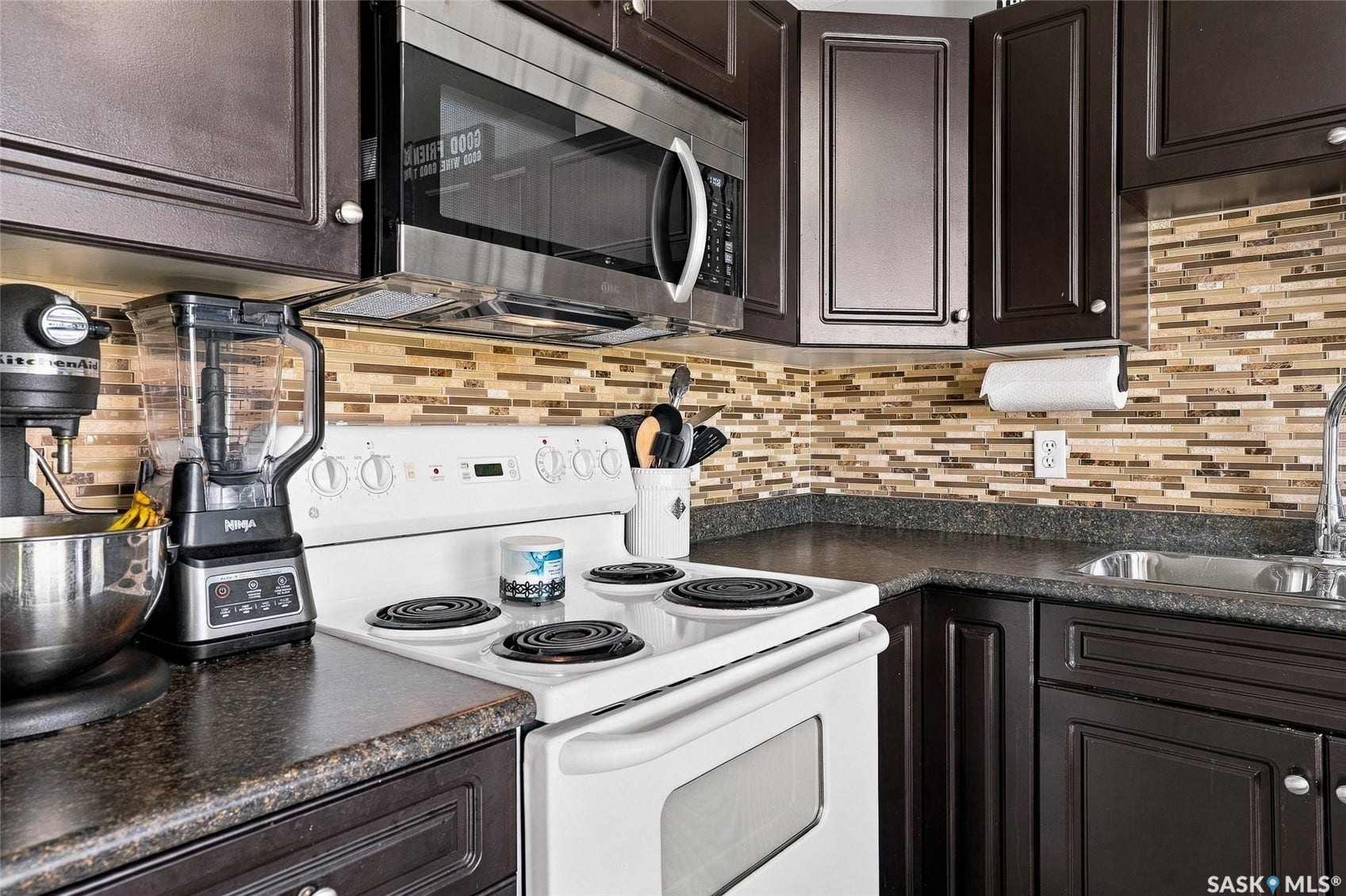 Kitchen featuring dark wood-finish cabinetry, a mosaic tile backsplash, dark countertops, and a stainless steel over-the-range microwave