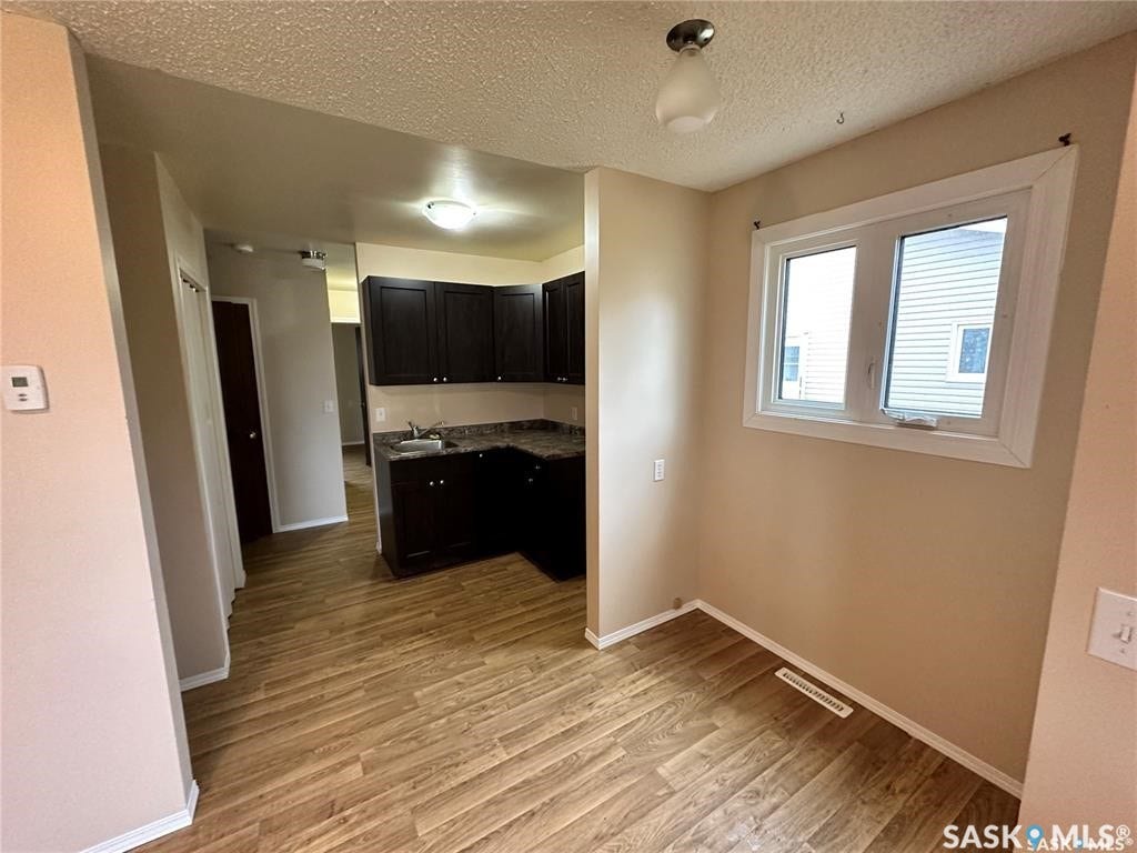Wood-finish flooring throughout, kitchen with dark wood cabinetry and dark stone-finish countertops, white-framed window