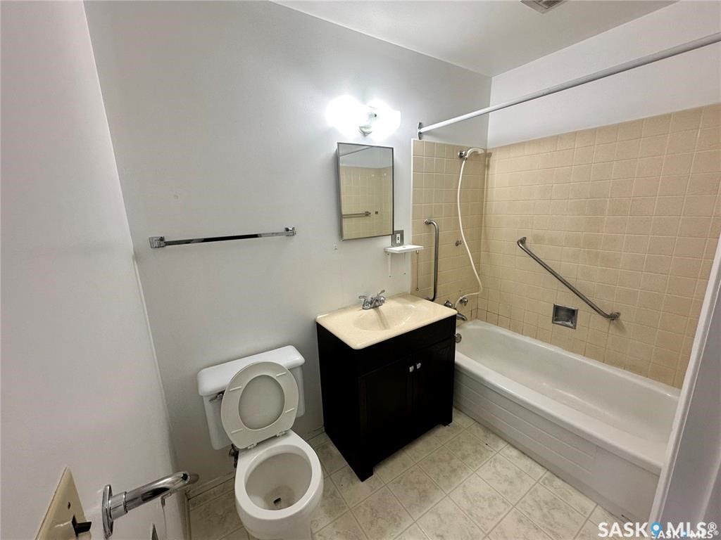 Bathroom featuring a dark wood-finish vanity, integrated sink, and a tiled tub surround with grab bars