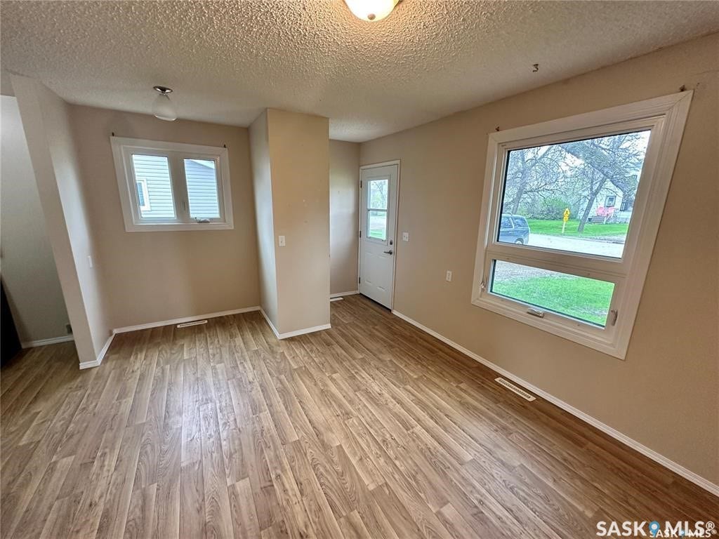 Wood-finish flooring throughout, multiple windows with white trim, neutral wall color, and a white entry door