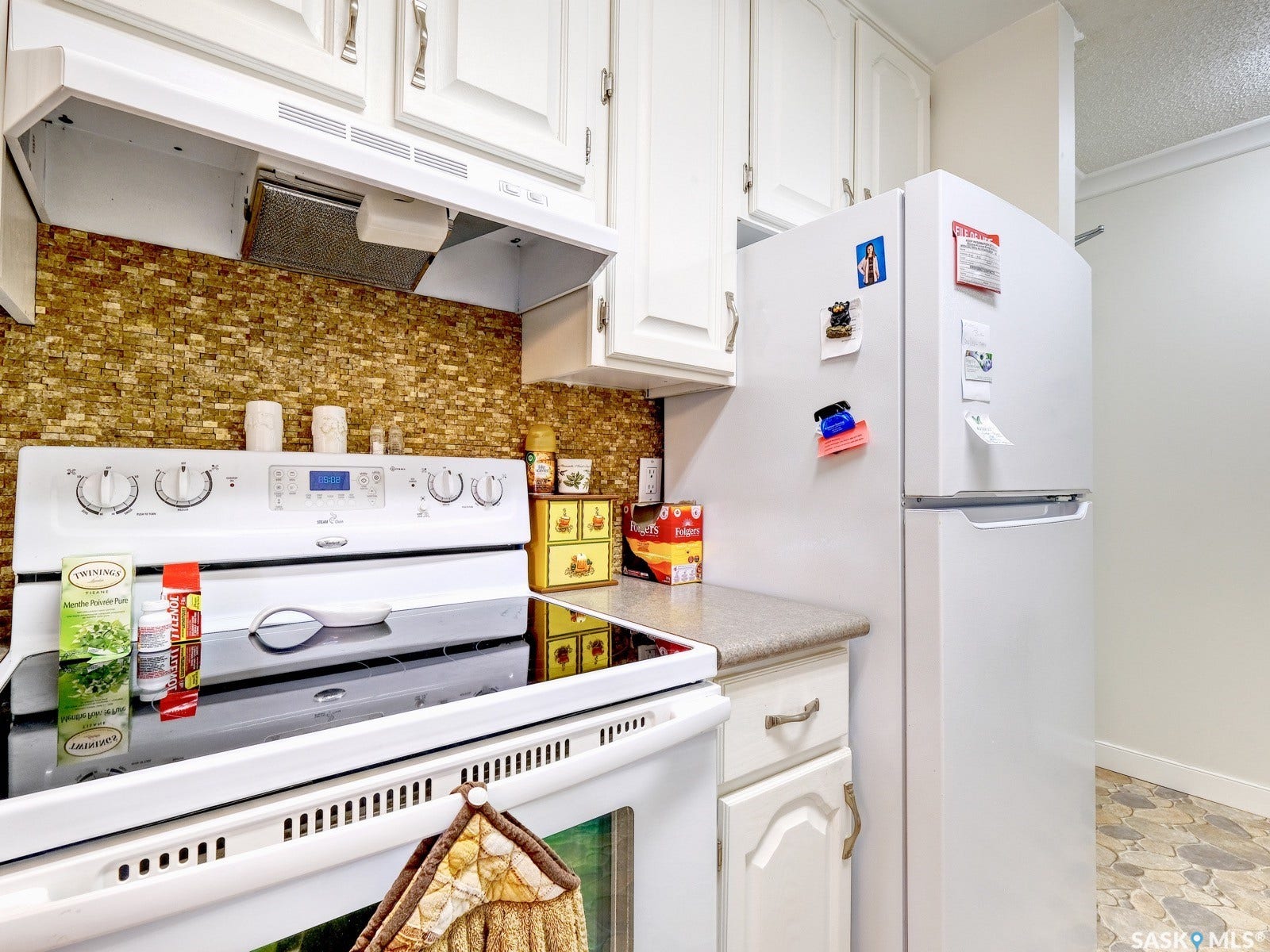 305 1st Street W, #302, Rosetown SK S0L 2V0 White upper and lower cabinetry, textured tile backsplash, solid surface countertops, and a white freestanding range with a flat cooktop