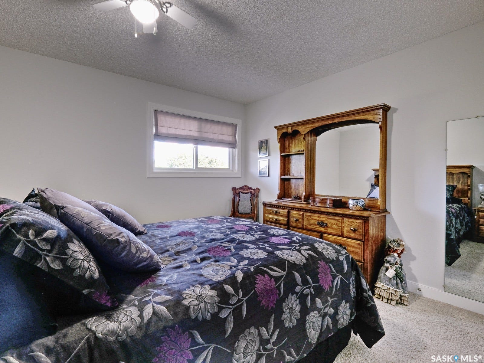 305 1st Street W, #302, Rosetown SK S0L 2V0 Textured ceiling, ceiling fan with integrated lighting, window with privacy blind, wood-finish dresser with integrated mirror, and wall-to-wall carpeting