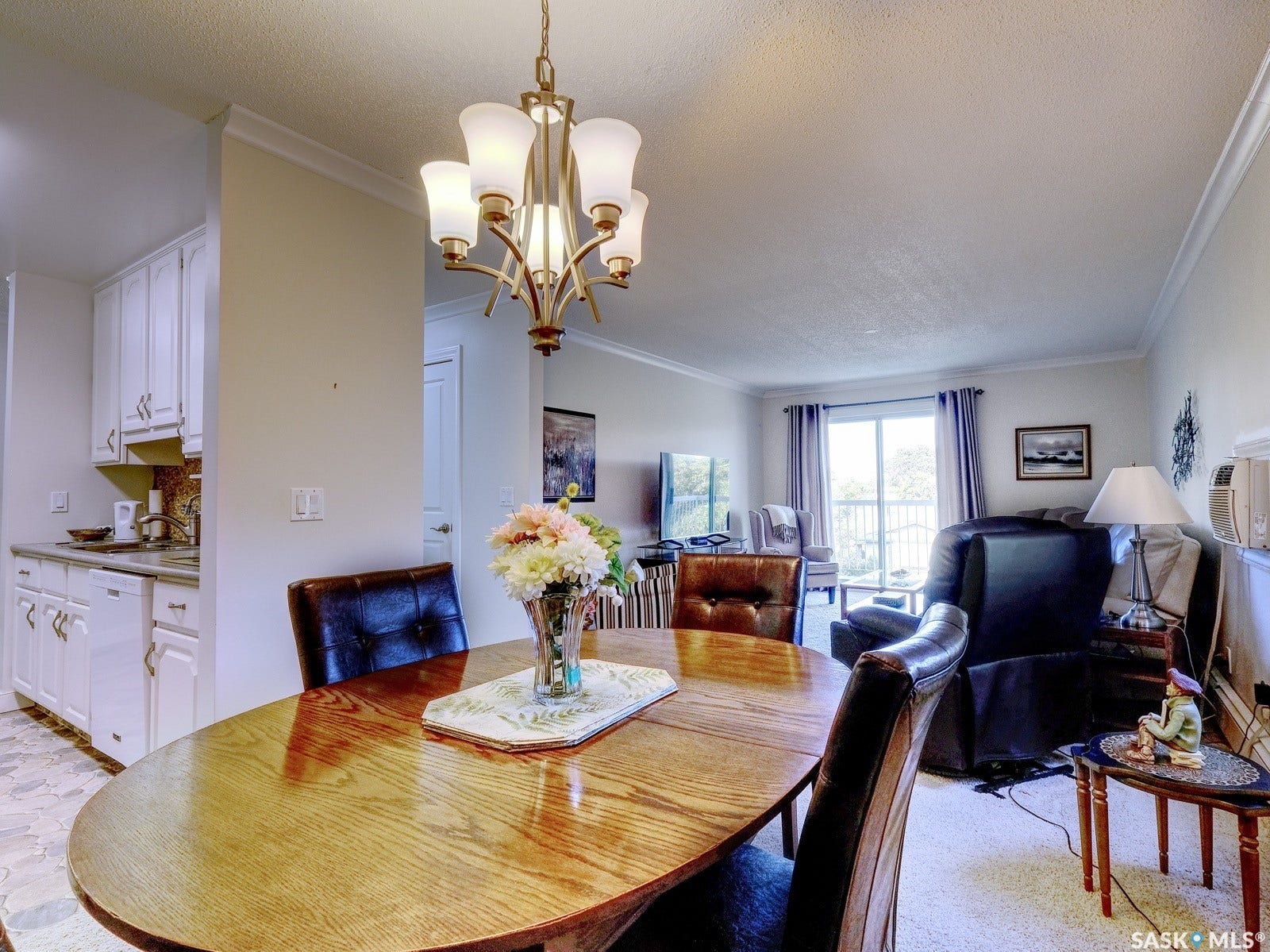 305 1st Street W, #302, Rosetown SK S0L 2V0 Hardwood dining table with a multi-light chandelier, crown molding, and a sliding glass door to the exterior