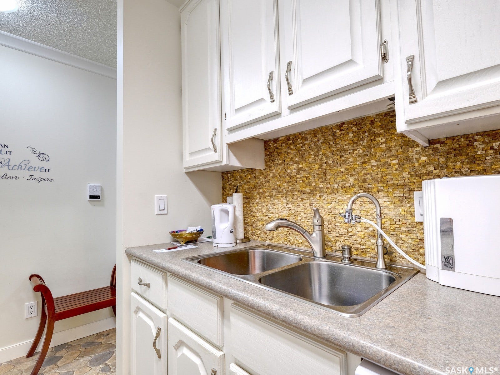 305 1st Street W, #302, Rosetown SK S0L 2V0 White cabinetry with brushed nickel hardware, mosaic tile backsplash, double basin stainless steel sink, and light-toned countertop