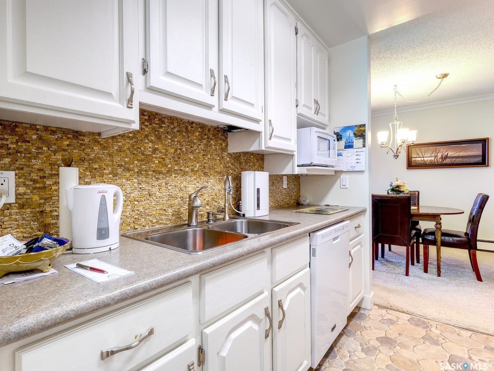 305 1st Street W, #302, Rosetown SK S0L 2V0 White cabinetry with brushed nickel hardware, mosaic tile backsplash, double basin stainless steel sink, and light-toned countertops