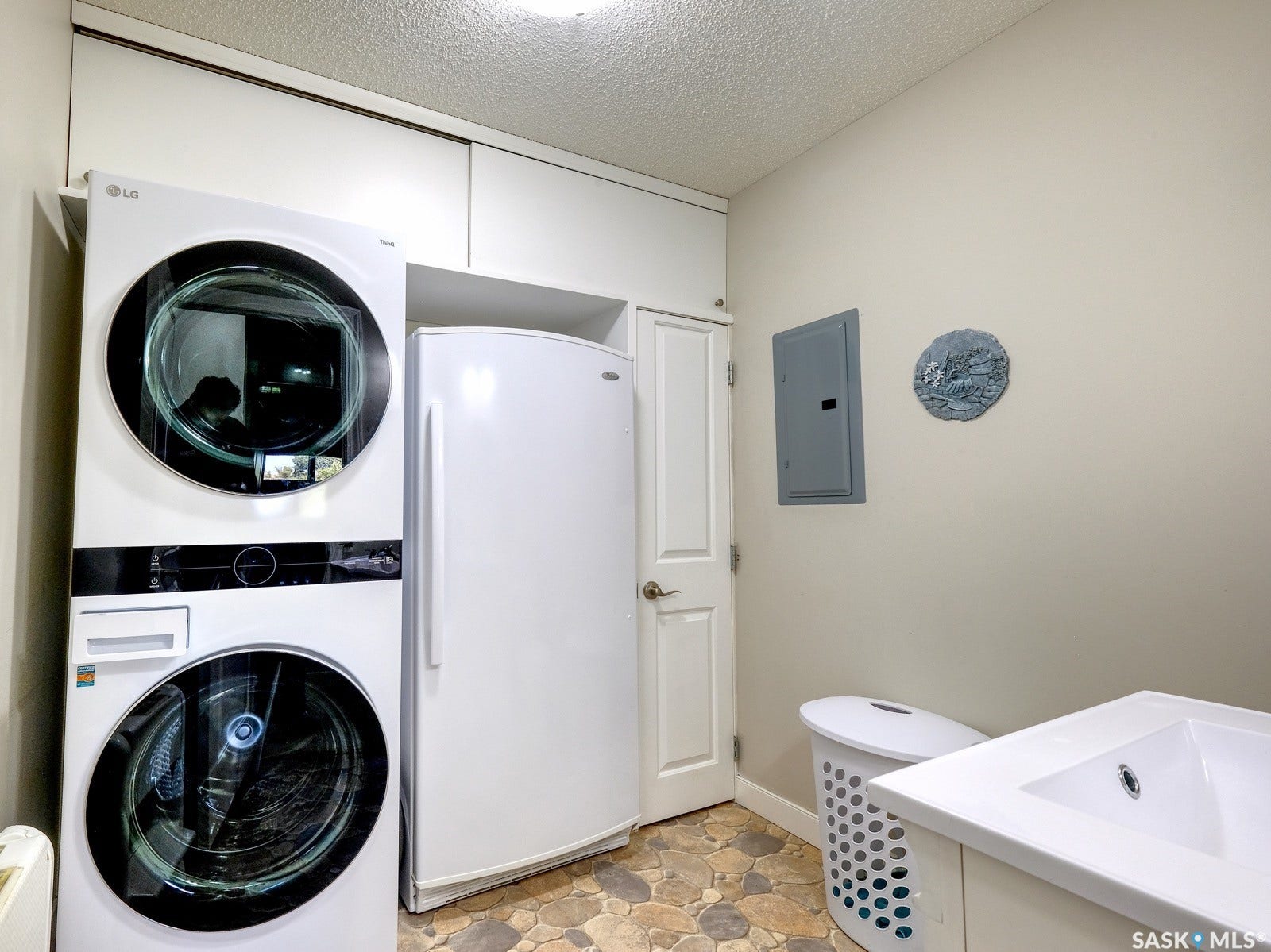 305 1st Street W, #302, Rosetown SK S0L 2V0 Stacked washer and dryer unit, built-in cabinetry, additional white refrigerator, integrated sink in vanity, and stone-look flooring