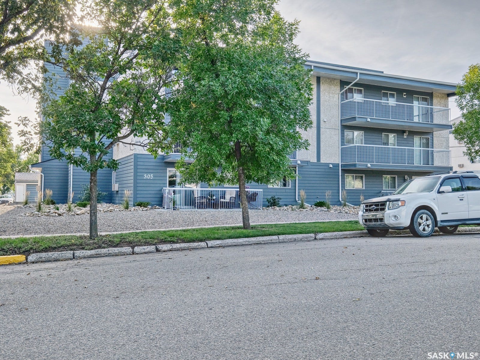 305 1st Street W, #302, Rosetown SK S0L 2V0 Multi-story building featuring balconies with glass railings, blue paneling, and stucco accents