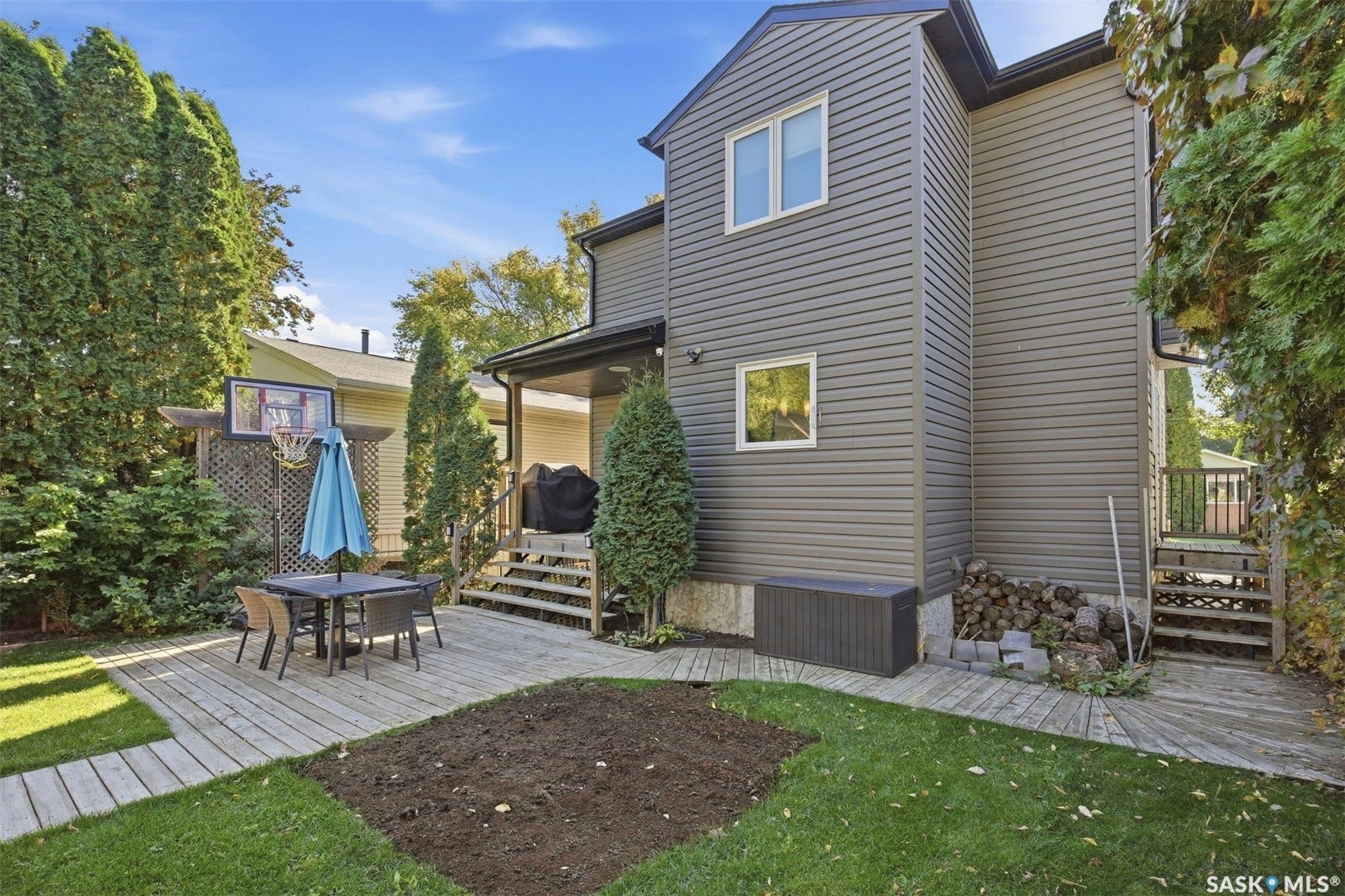 Manicured lawn, wood decking, covered patio, horizontal siding, and mature perimeter landscaping