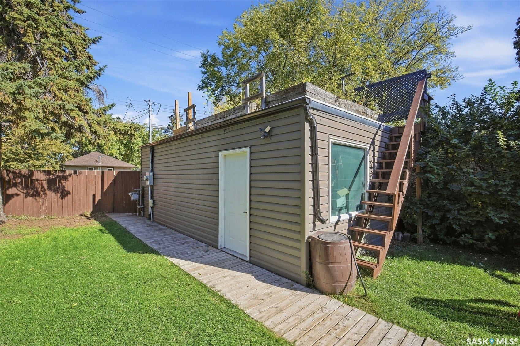 Detached auxiliary structure featuring siding, a secure entry door, and an exterior staircase leading to a rooftop area