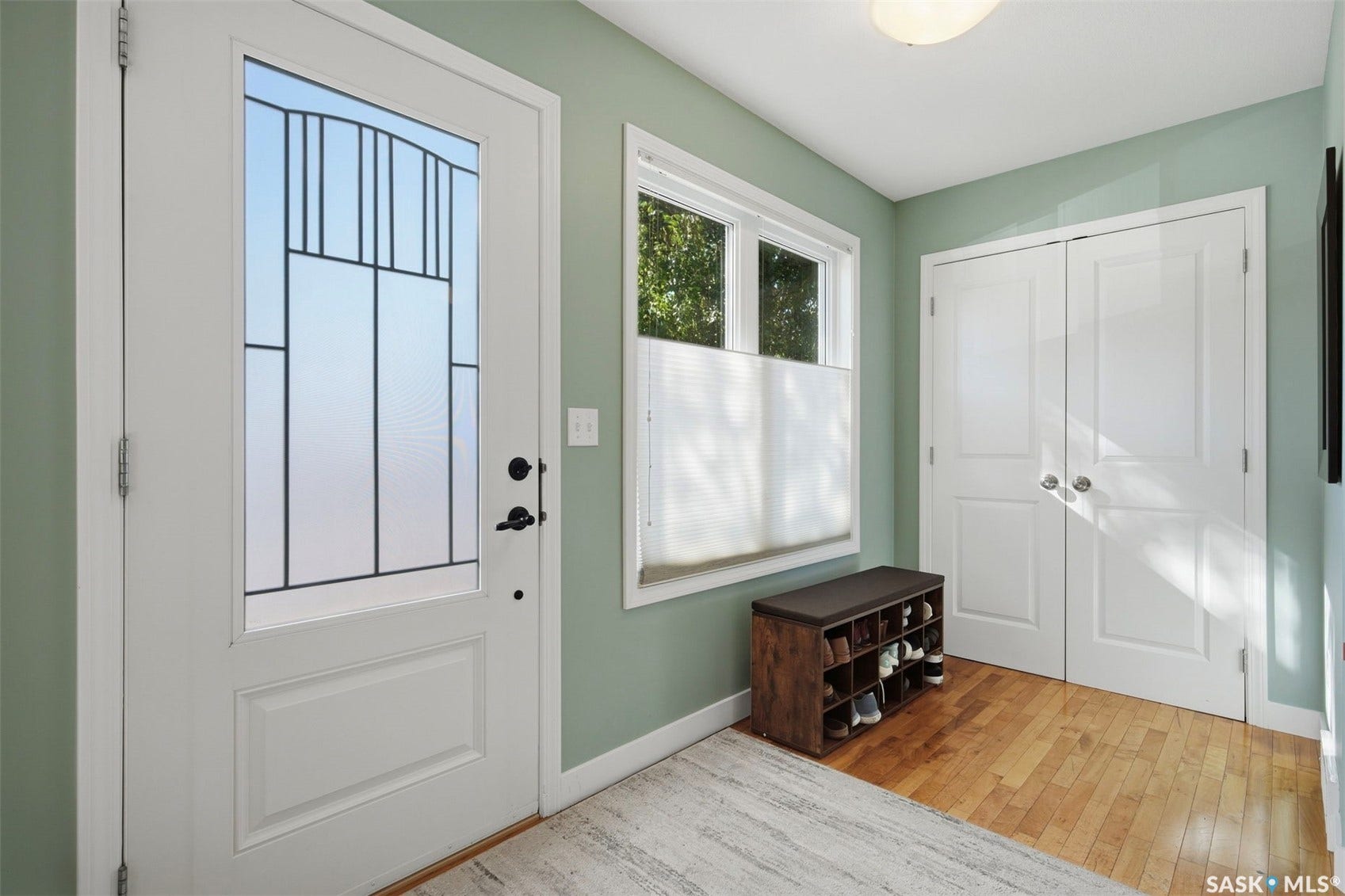 Entryway featuring a decorative glass panel door, light-toned wood-finish flooring, a window with a cellular shade, and double bi-fold doors