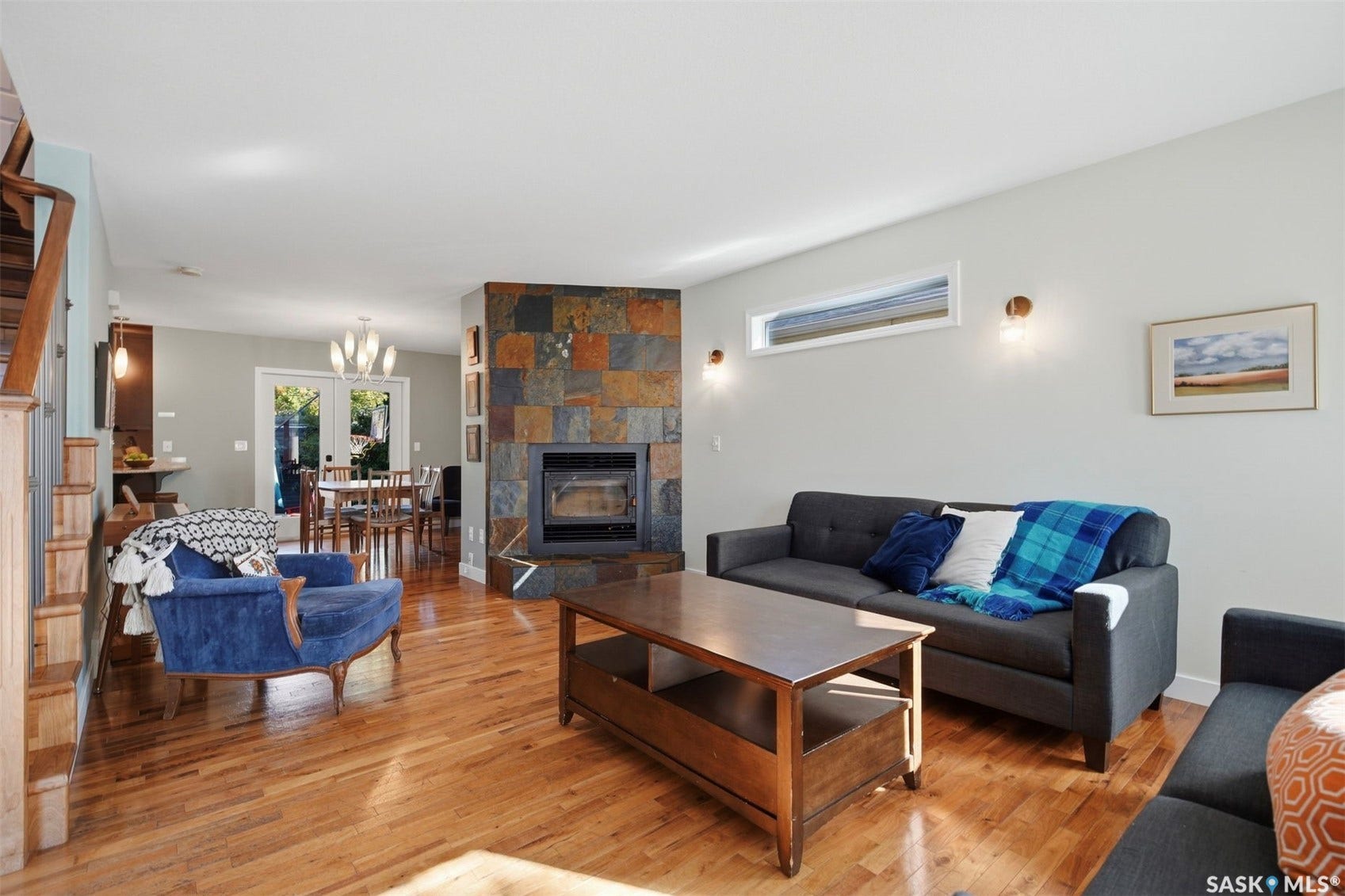 Hardwood flooring, a natural stone fireplace, a rectangular transom window, and dual wall sconces