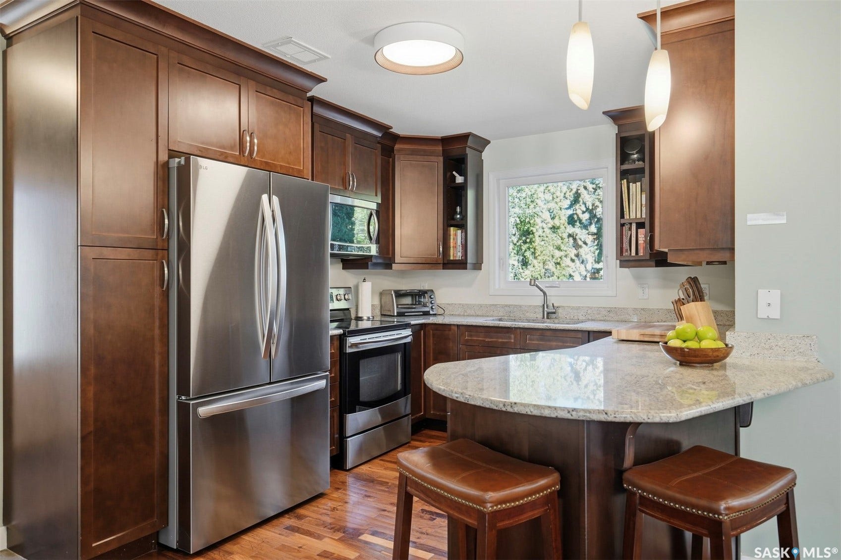Kitchen featuring rich wood cabinetry, stainless steel appliances, granite countertops, and wood-finish flooring