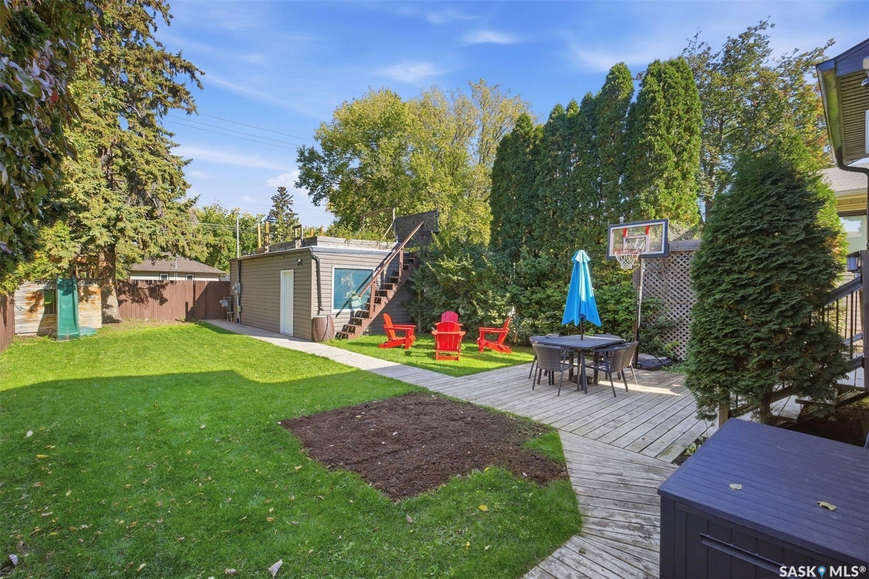 Expansive backyard featuring a large grass area, wood-finish deck, and mature privacy trees