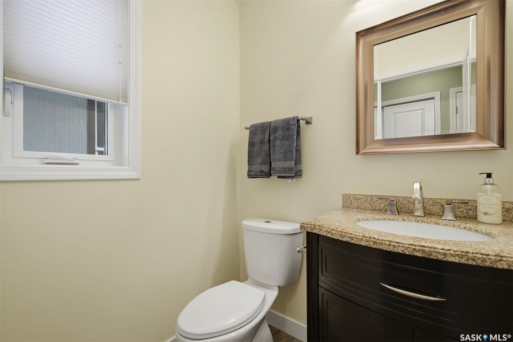 Granite countertop, undermount sink, dark wood vanity with brushed nickel hardware, and framed mirror