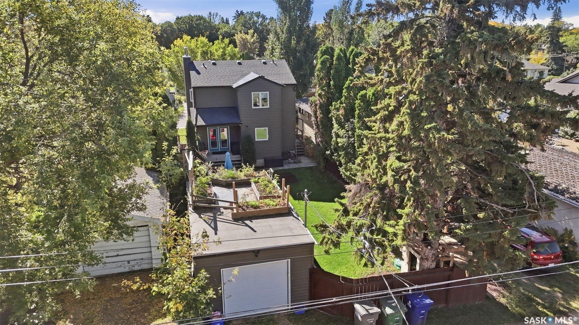 Two-story residence with a dark gray exterior, a detached garage featuring a flat roof and white garage door, and an expansive backyard with a manicured lawn