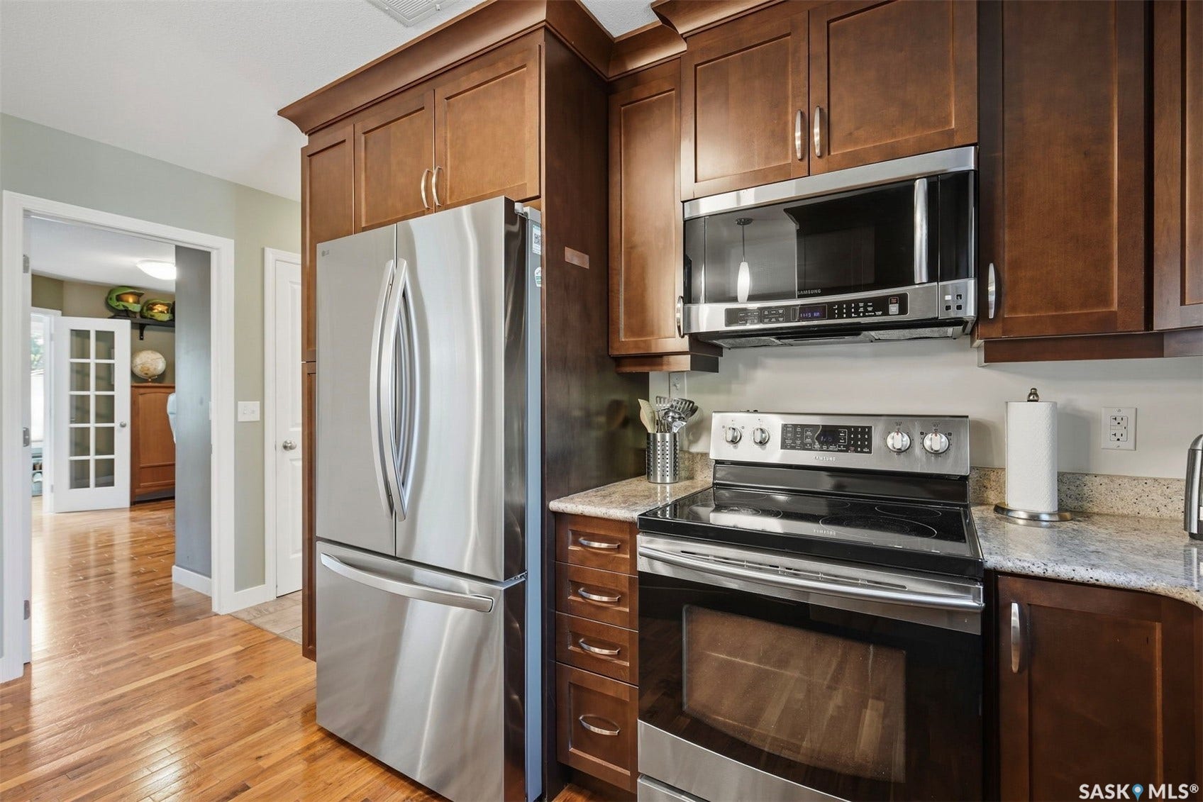 Stainless steel French door refrigerator, stainless steel electric range, stainless steel microwave, wood cabinetry, and light-toned countertops