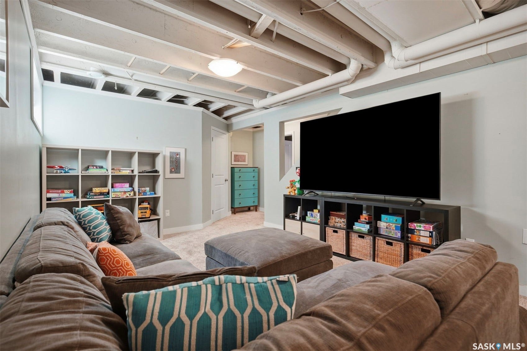 Finished basement space featuring exposed white ceiling joists, light blue wall paint, and beige carpeting