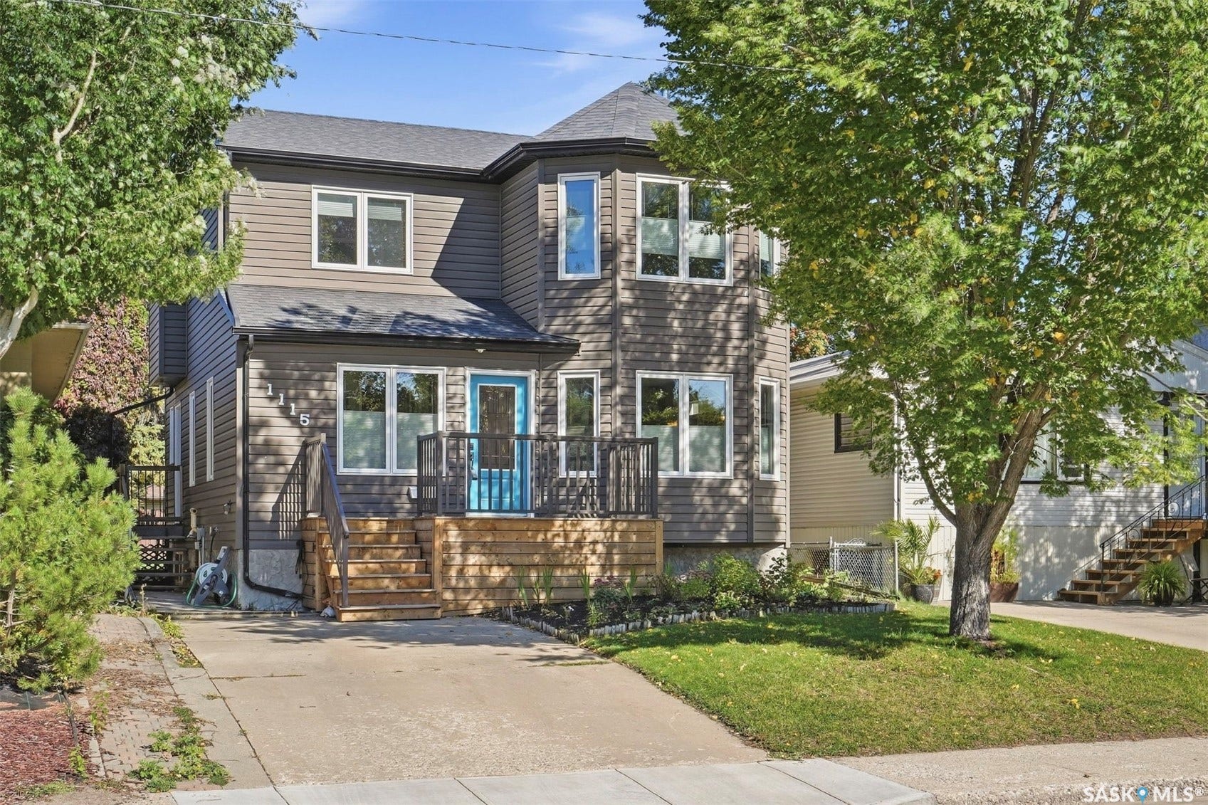 Modern exterior with dark siding, white window trim, a vibrant blue entry door, and an inviting front deck