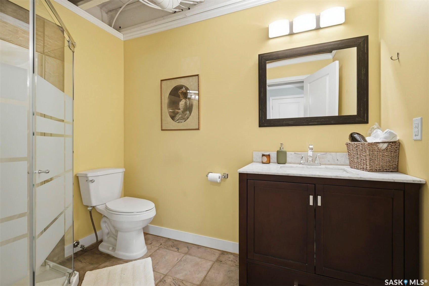 Bathroom featuring a standing shower with frosted glass, a vanity with a white countertop and dark wood-finish cabinetry, and a framed mirror with overhead lighting