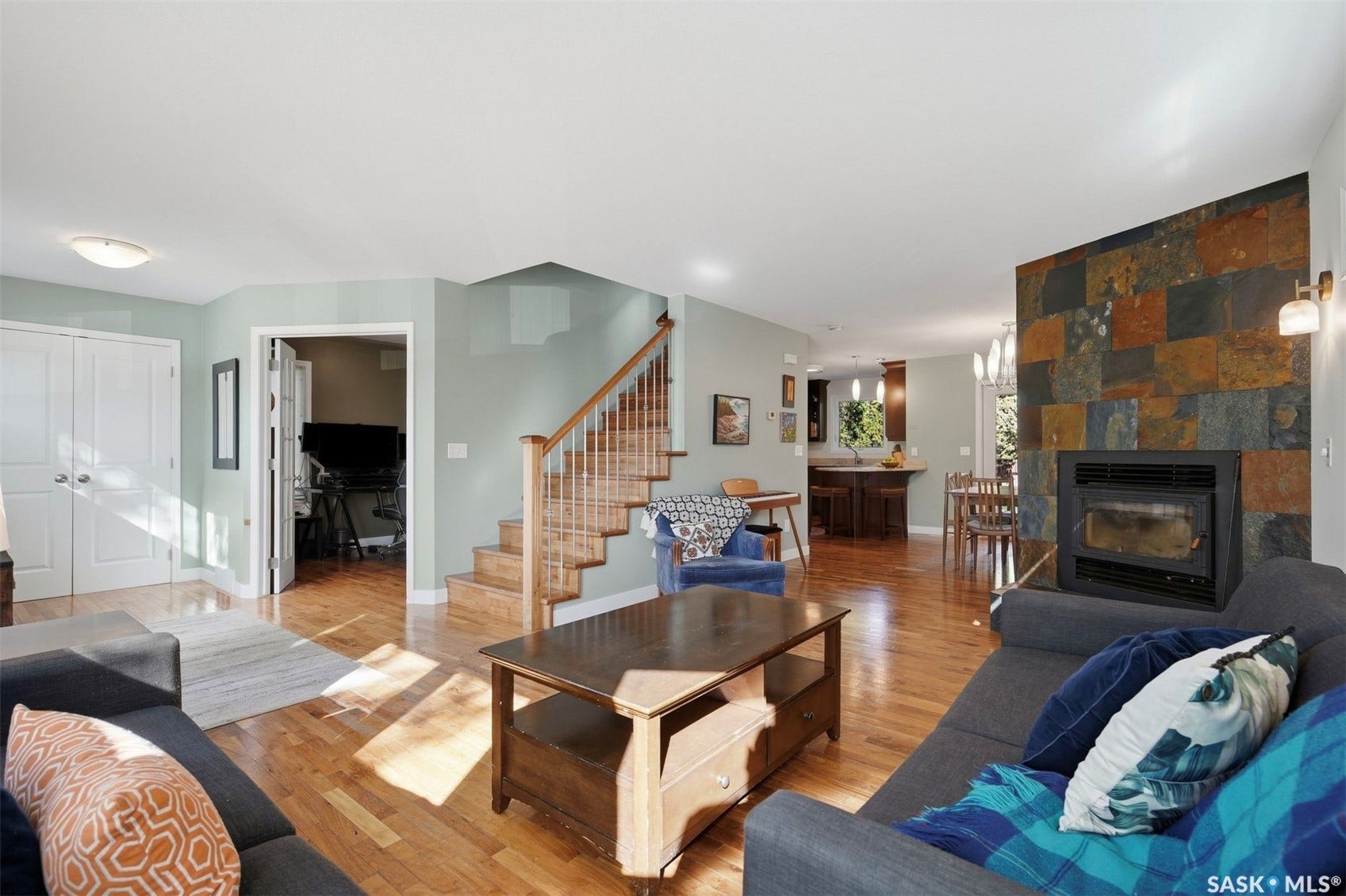Hardwood flooring, multi-toned slate-clad fireplace, open-tread staircase with wood railings, double-door entry, and recessed lighting