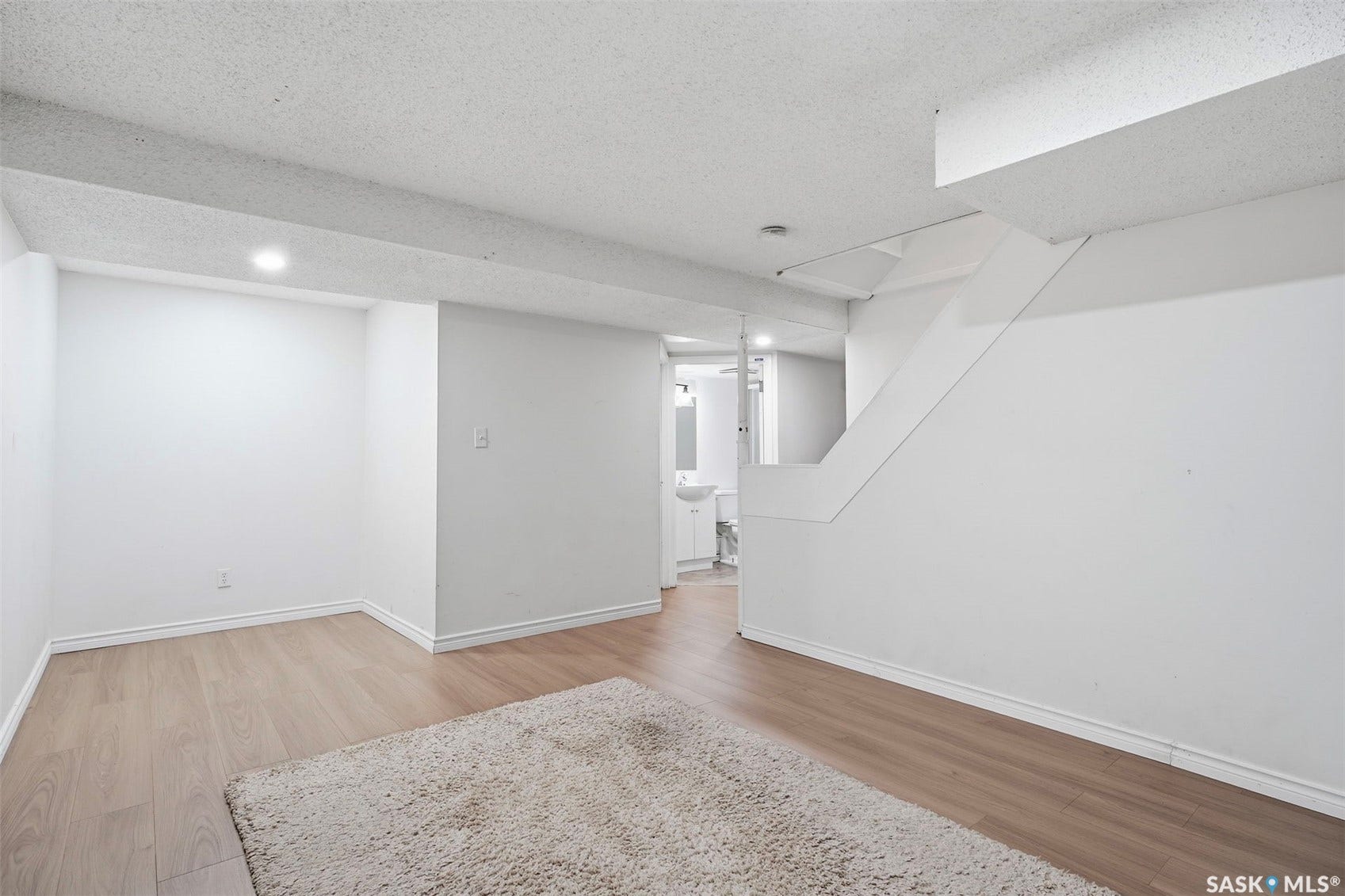 Light wood-finish flooring, recessed ceiling lighting, a white painted staircase, and a white built-in vanity with a circular basin sink