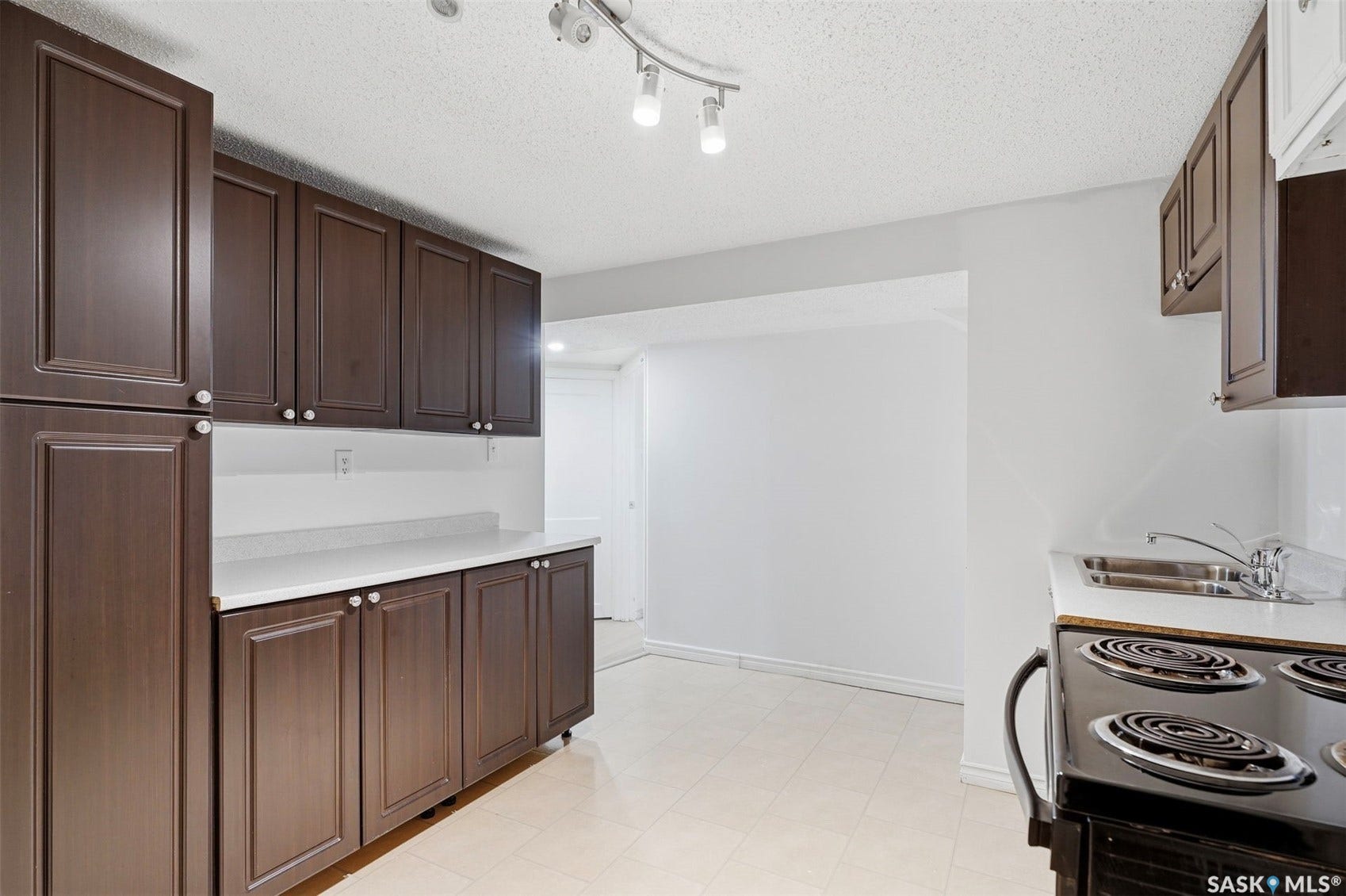 Kitchen featuring dark wood-finish cabinetry, white countertops, a stainless steel sink, and a black electric range