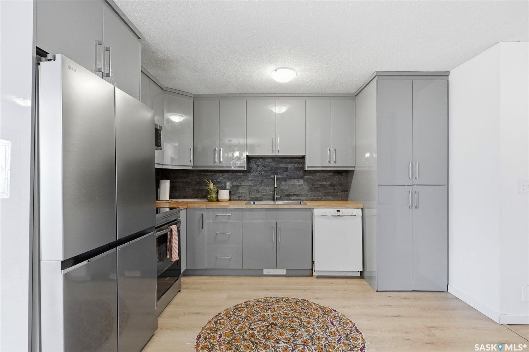 Sleek kitchen featuring gray cabinetry, stainless steel refrigerator, dark tile backsplash, wood-finish countertops, and light wood-finish flooring