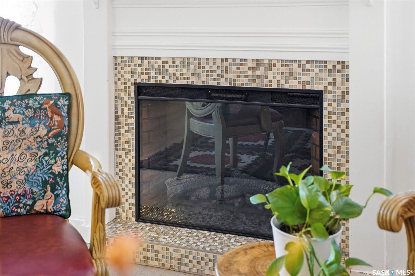 Elegant living space featuring a wood-burning fireplace with a mosaic tile surround in warm neutral tones, complemented by ornate gilt-framed mirror and upholstered seating with decorative pillow detailing