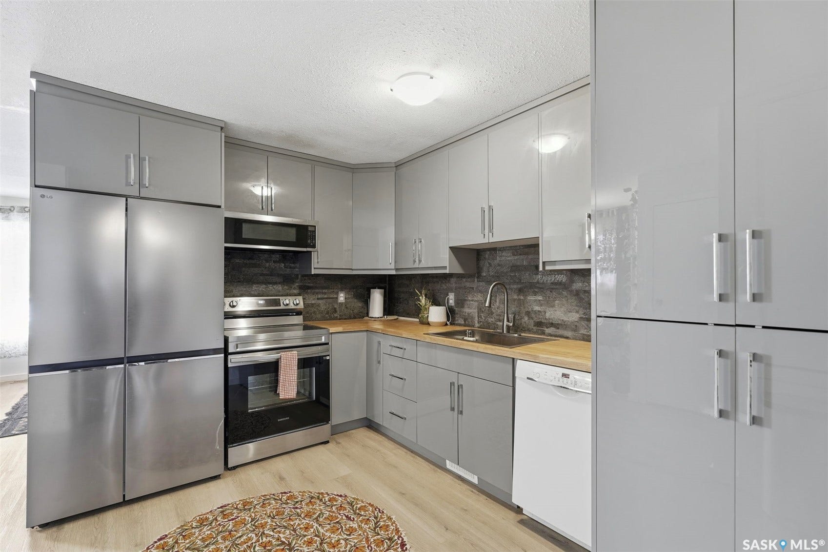 Modern kitchen featuring light gray cabinetry, stainless steel appliances, wood-finish countertops, and light wood-finish flooring