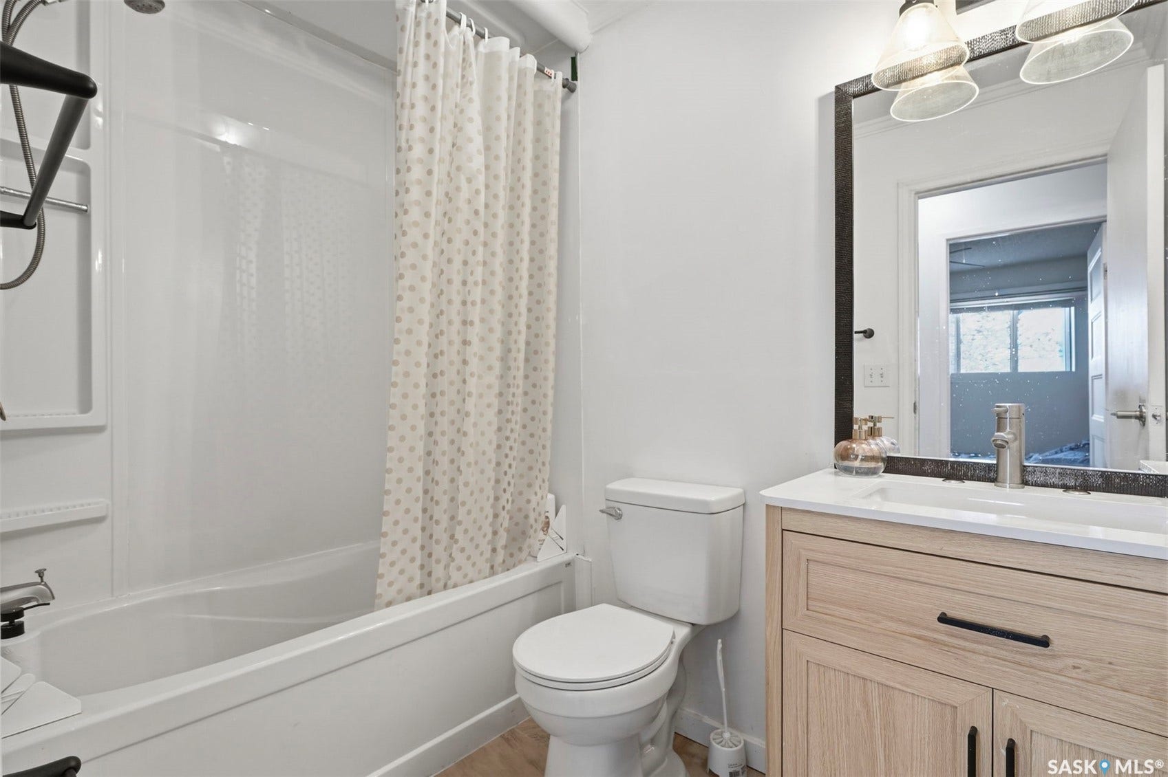 White tub/shower combination, light wood-finish vanity with countertop, rectangular undermount sink, and wall-mounted mirror with integrated lighting