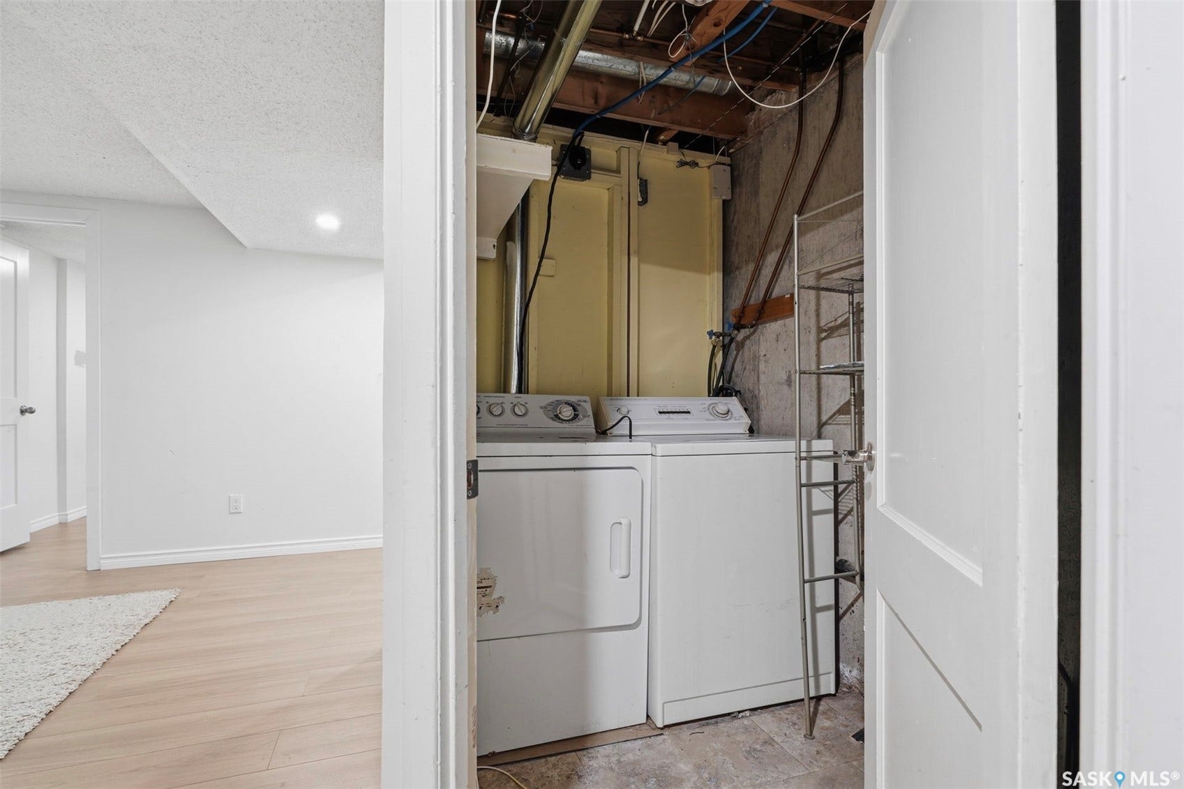 Laundry area featuring a side-by-side washer and dryer, adjacent to a finished room with light wood-finish flooring