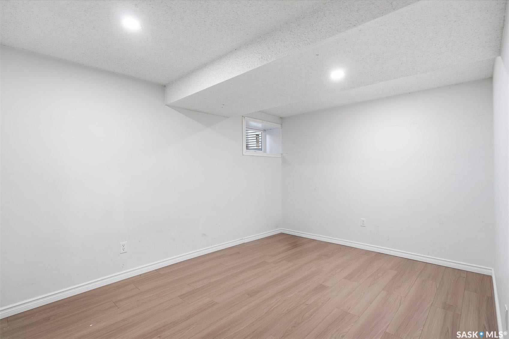 Recessed lighting illuminating the space, wood-finish flooring, white wall paint, and a small window